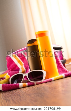 Sun protection cosmetics and sunglasses on striped towel next to a bag.