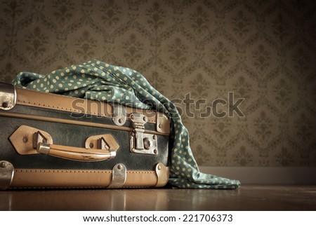 Vintage elegant suitcase on floor with dotted clothing and vintage wallpaper on background.