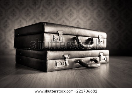 Stack of leather briefcases with vintage wallpaper background.
