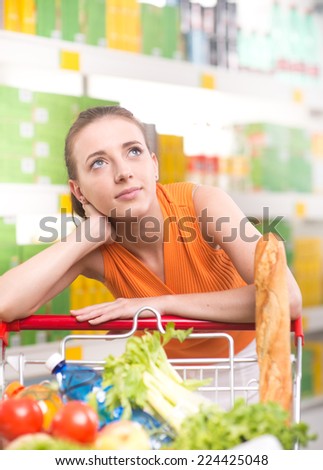 Pensive young woman at store looking up with supermarket shelves on background.