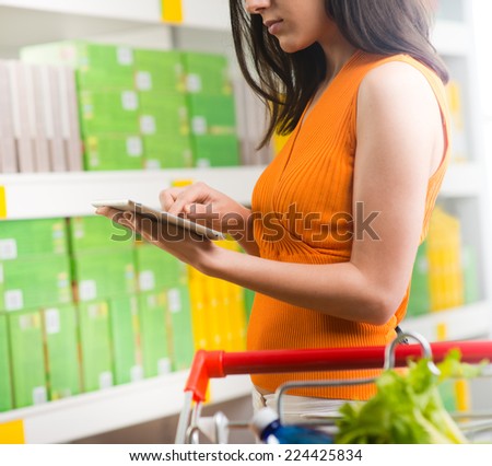 Young woman using a digital tablet at store with supermarket shelves on background.