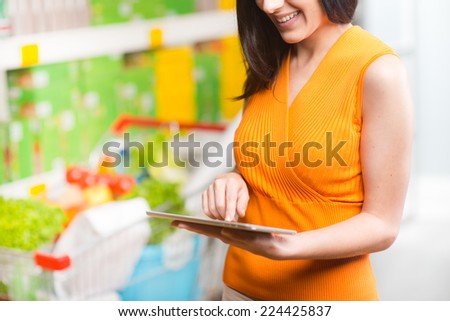 Young woman at supermarket shopping with digital tablet and shelves on background.