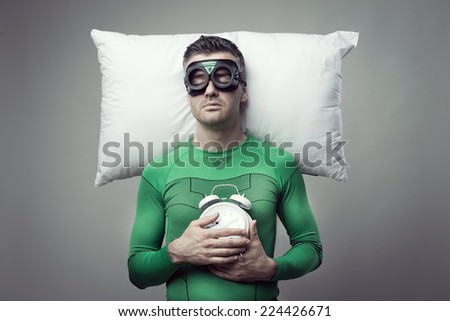 Superhero sleeping on a pillow floating in the air holding alarm clock.