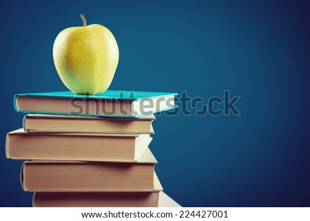 Back to school with pile of books and yellow apple on blue background.