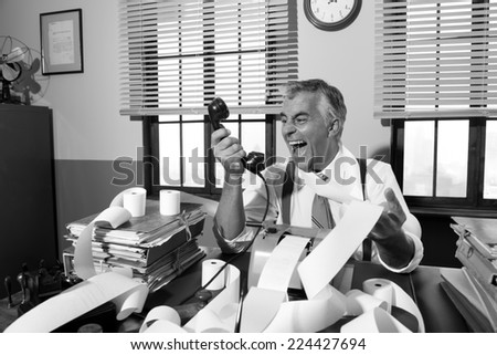 Angry vintage businessman shouting out loud at phone surrounded by adding machine tape.