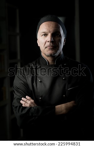 Confident chef posing with arms crossed on dark background.