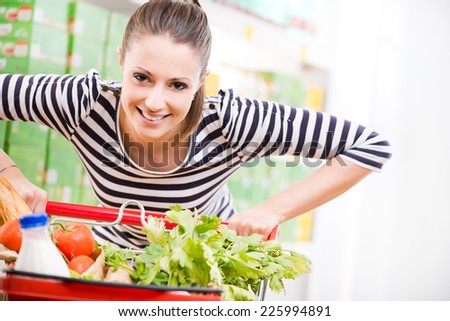 Attractive young woman smiling and pushing a cart at supermarket.