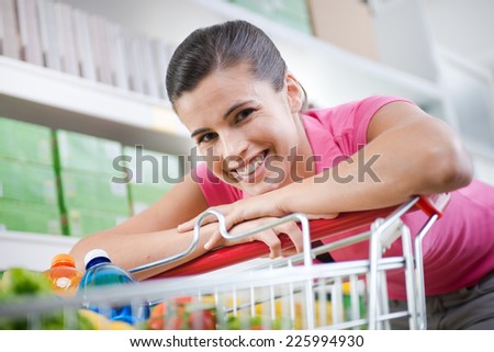 Young woman in pink shirt leaning to a shopping cart at supermarket.