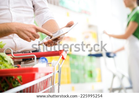 Customer using a digital tablet at supermarket with sales clerk on background.