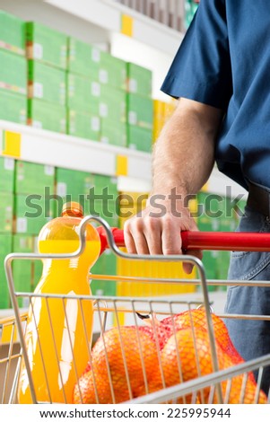 Man shopping at supermarket, hands on trolley close-up.