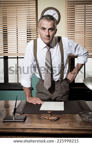 Aggressive businessman with arms akimbo staring confidently at camera, vintage office.