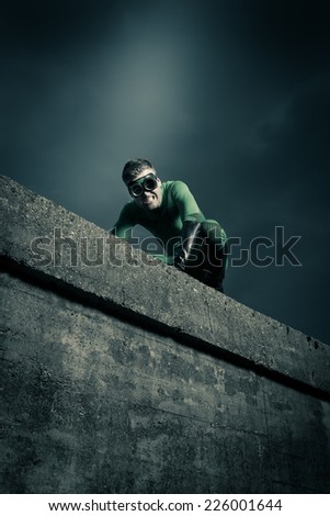 Green superhero on all fours escaping danger on a concrete wall.