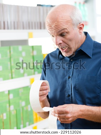 Shocked senior man checking astonishing prices on a long grocery receipt.