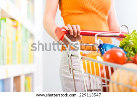 Woman shopping at supermarket, hands on trolley close-up.