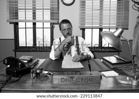 Pensive director with hand on chin working at office desk, 1950s style.