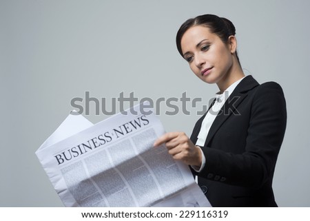 Attractive confident businesswoman with black jacket holding financial newspaper.