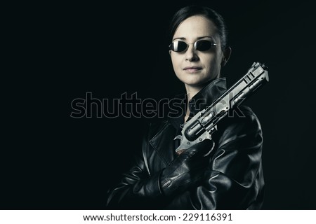 Attractive female agent in black leather coat and sunglasses holding a gun.