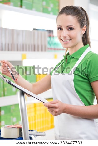 Attractive female sales clerk at work holding a clipboard with supermarket shelf on background.