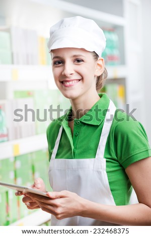 Young female sales clerk posing with digital tablet at supermarket.