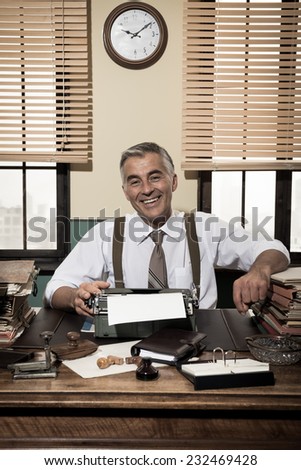 Cheerful vintage office worker sitting at desk and smiling at camera.