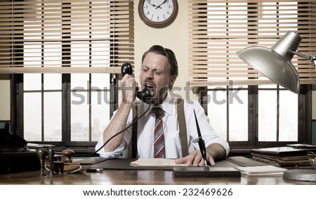 Angry vintage businessman shouting on the phone working at office desk.