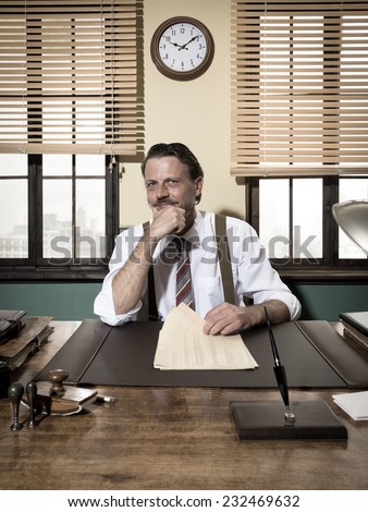 Confident smiling businessman working at office desk with hand on chin.