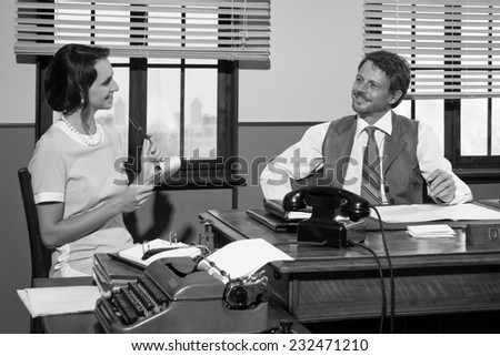 Director and secretary working together at desk, 1950s style office.