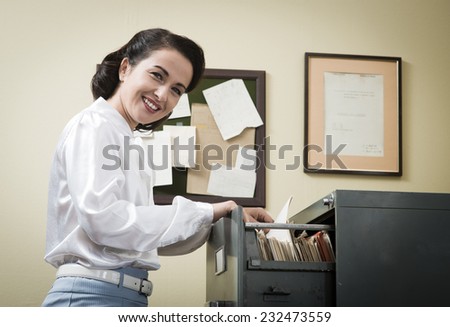Smiling vintage secretary searching files in the filing cabinet drawers