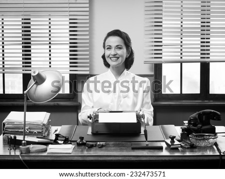 Cheerful vintage secretary working at office desk and smiling at camera