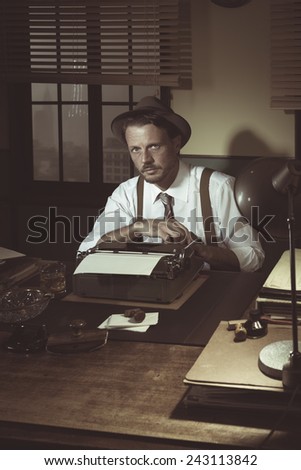 Retro reporter sitting at desk with typewriter posing and looking at camera.