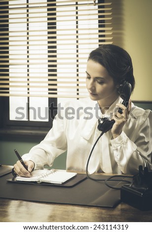 Professional vintage secretary on the phone writing down appointments and taking notes