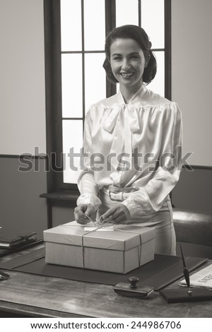 Smiling secretary holding a mail package with rope and label, 1950s style