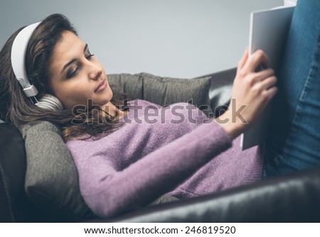 Young  relaxed woman on sofa with headphones reading a book