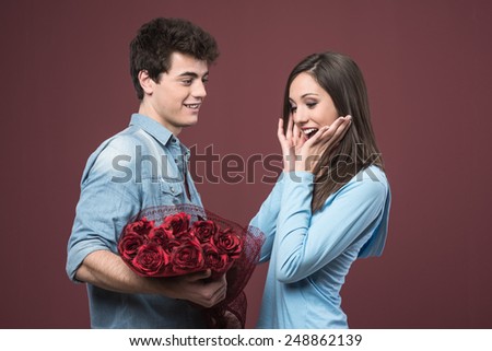 Smiling young woman receiving red roses as love gift from her boyfriend
