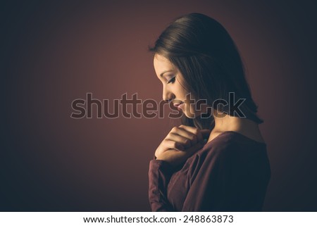 Beautiful young woman looking down, profile on dark background
