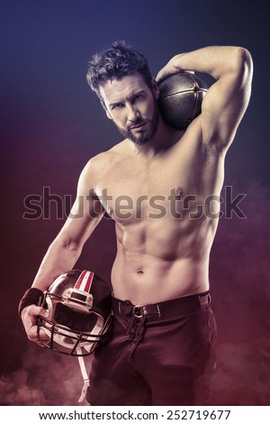 Attractive shirtless football player holding protective helmet and posing