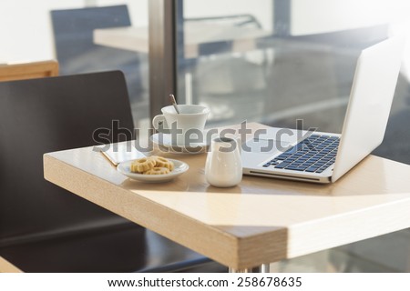 Table at the cafe with a cup of coffee, cookies and a laptop next to a window