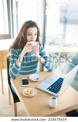 Beautiful girl drinking a coffee at the bar and connecting with a computer
