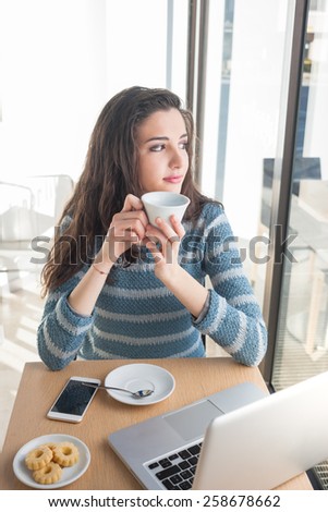Beautiful girl drinking a coffee at the bar and connecting with a computer