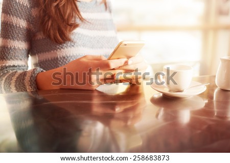 Woman leaning on the bar counter and text messaging with her mobile, hands close up