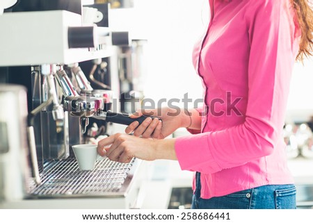 Young waitress making coffee with an espresso coffee machine, she is holding a cup and the filter holder