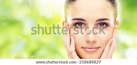 Beautiful female model touching her smooth glowing face skin and smiling at camera