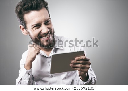 Cheerful smiling man receiving good news on tablet with fist raised