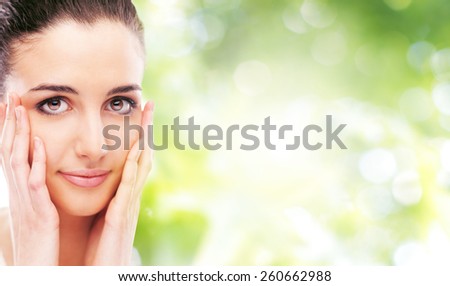 Beautiful female model touching her smooth glowing face skin and smiling at camera