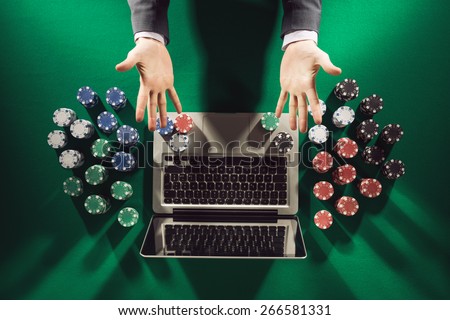 Online player\'s hands palms up with laptop and stack of chips all around on green table top view
