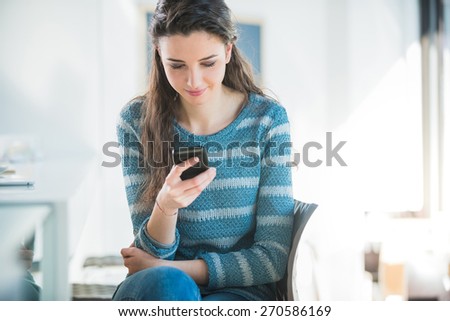 Smiling beautiful teenager girl sitting at the bar counter and texting with her mobile phone