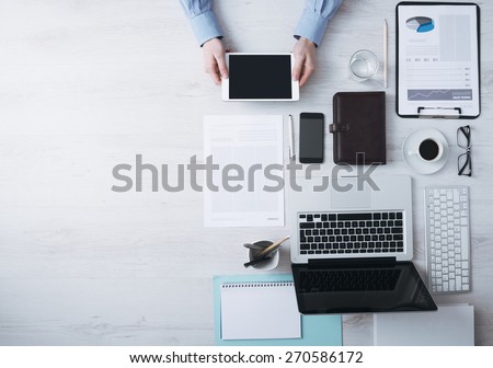 Businessman working at office desk and using a digital touch screen tablet hands detail, computer and objects on the right, top view