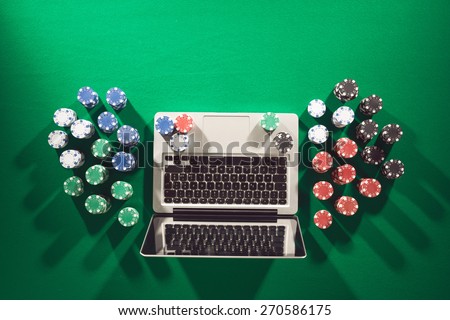Poker and casino online gaming concept with laptop and stacks of chips on green table, top view