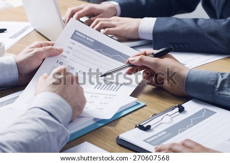 Business professionals working together at office desk, hands close up pointing out financial data on a report
