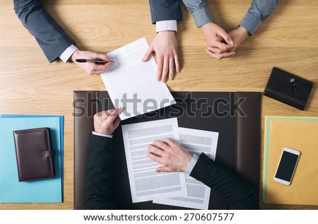 Business man and woman sitting at the lawyers\'s desk and signing important documents, hands top view, unrecognizable people